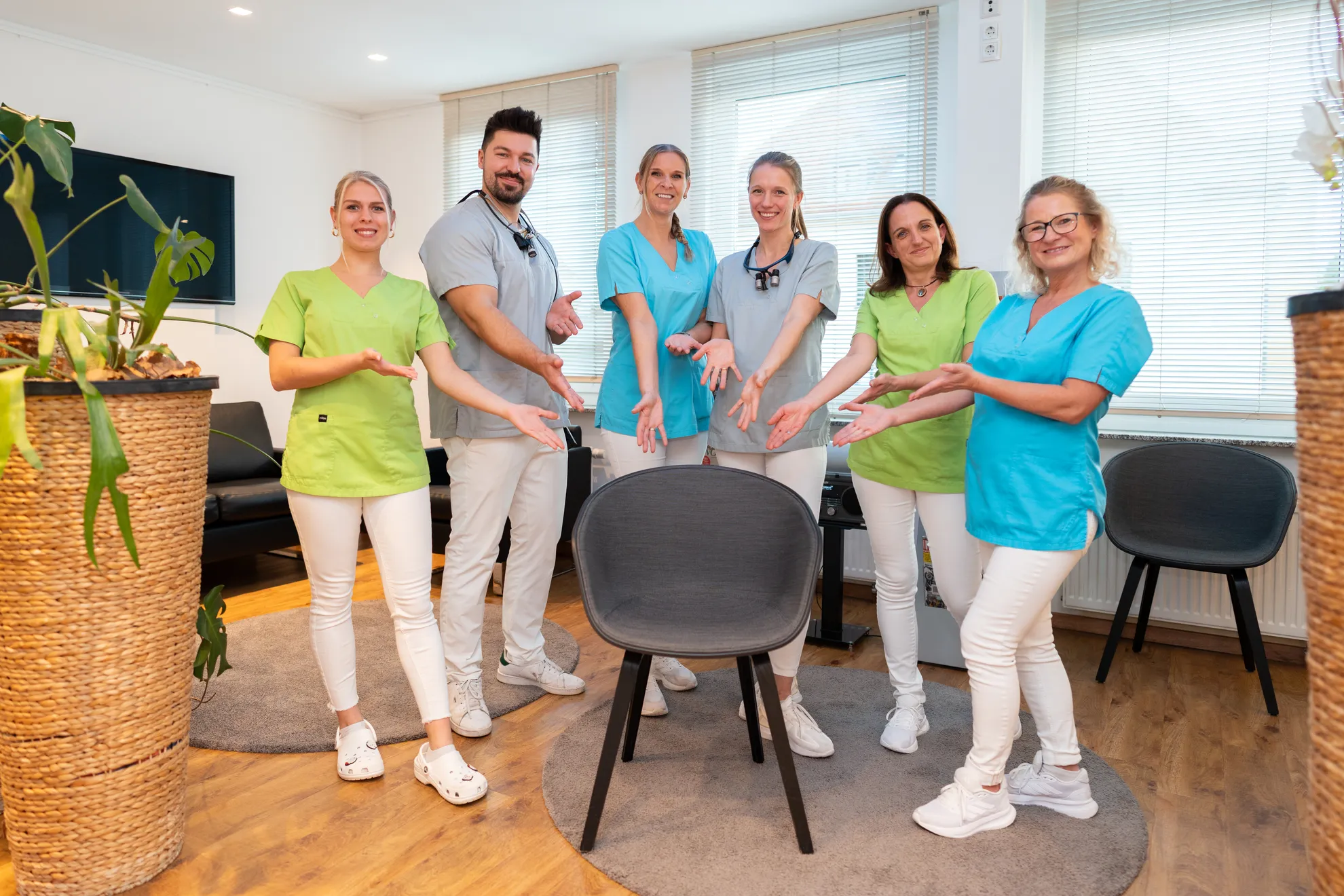 Das Team zeigt lächelnd auf einen Holzstuhl im Sinne von "Hier fehlst du, werde Teil des Teams"