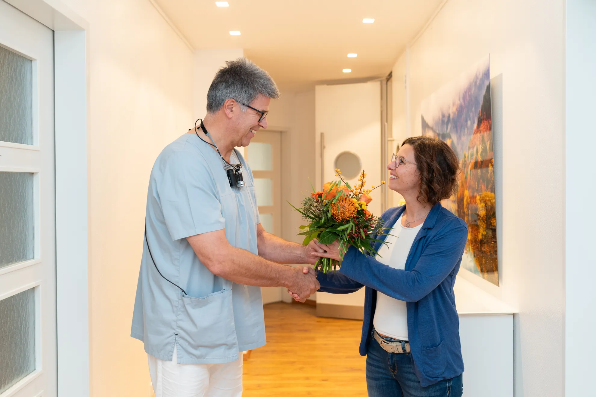 Zahnarzt überreicht der Kollegin einen Blumenstrauß, beide lächeln
